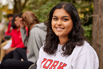 Smiling York student posing for a photo while wearing white sweater.